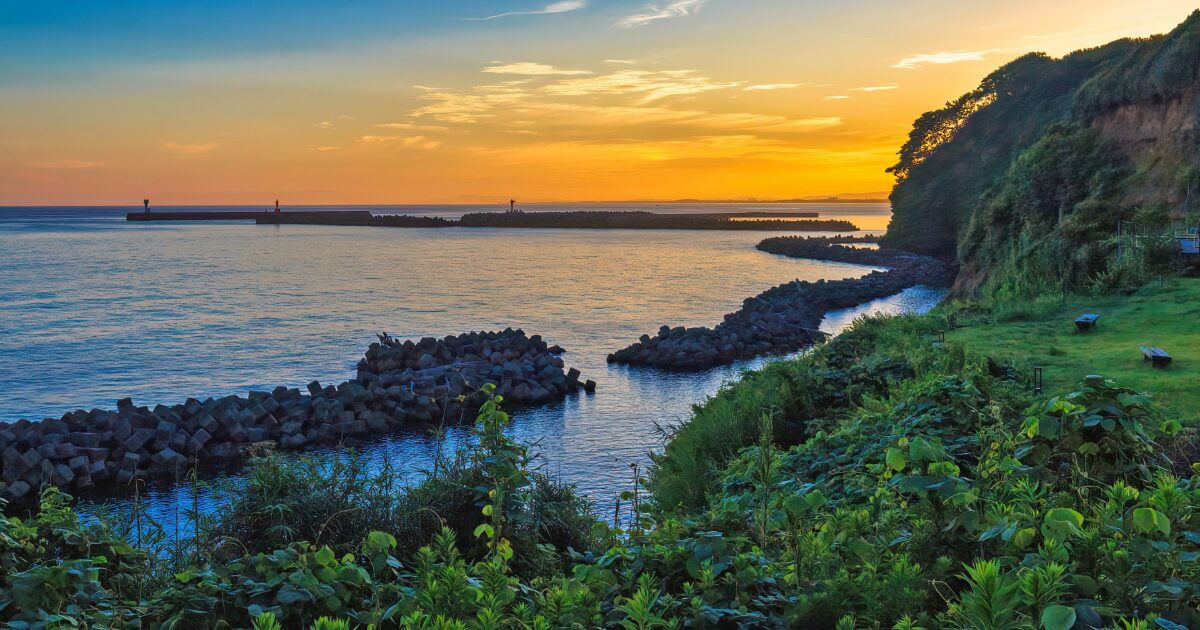 夕焼けに染まる日本海と防波堤の風景