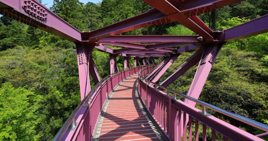 赤い鉄骨構造の歩道橋と周囲の森林風景